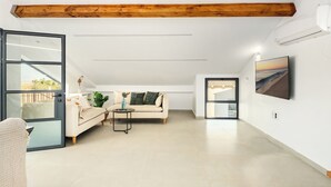Ein geräumiges Wohnzimmer mit hoher Decke, einem Holzbalken, einer Couch, einem Couchtisch und einem an der Wand befestigten Fernseher.