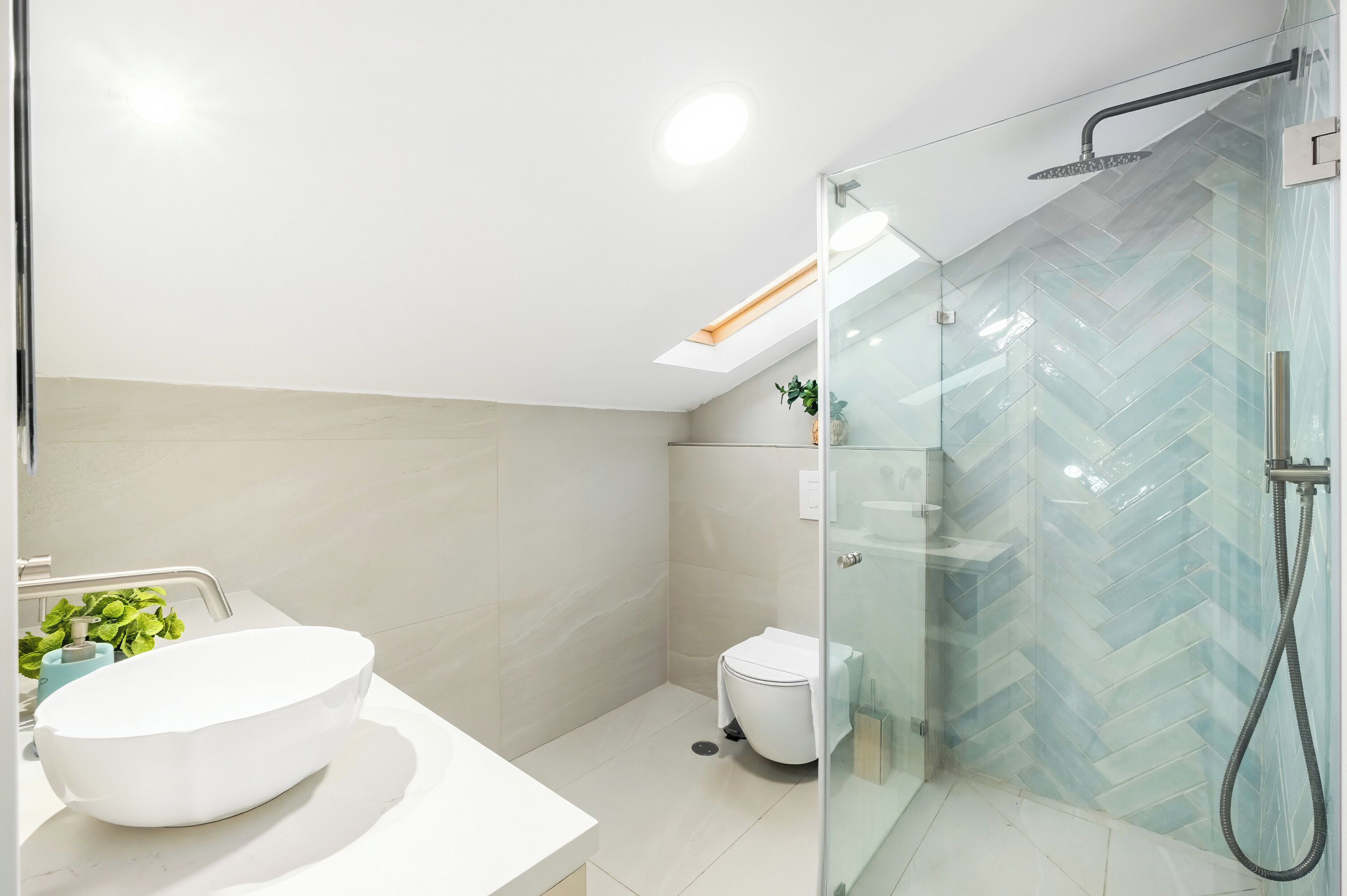 Un baño moderno con cabina de ducha de vidrio, un lavamanos blanco y un inodoro.