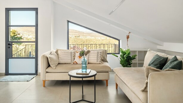 Ein modernes Wohnzimmer mit einer Couch, einem kleinen runden Tisch und einem großen Fenster mit Blick auf eine Landschaft.