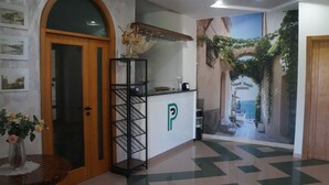 En lobby med reception, en trædør, en vægmonteret hylde og et flisegulv.