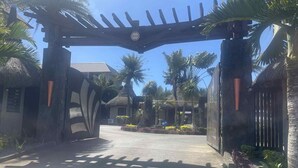 A tropical resort entrance with a wooden archway, palm trees, and a clear sky. - Résidences les Alizées (Grand-Baie)