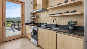 A modern kitchen with wooden cabinets, a stainless steel stove, and a black countertop. - 3BR Cabin 5 |Hot Tub + Pizza Oven +Fire Pit +Views (Marshall)