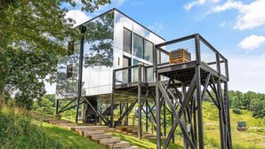 A modern house with a glass facade, wooden deck, and metal staircase. - 3BR Cabin 5 |Hot Tub + Pizza Oven +Fire Pit +Views (Marshall)