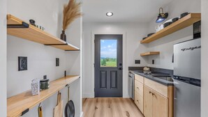 Una cocina moderna con estantes de madera, un refrigerador y vistas a través de la puerta.