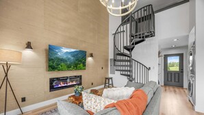 Una sala moderna con chimenea, un televisor de pantalla plana grande, una escalera y un área de lavandería.