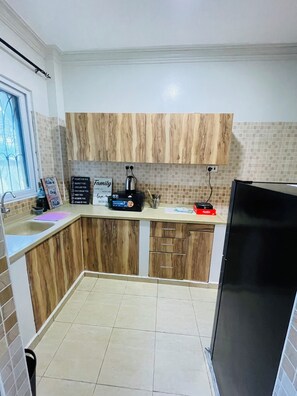 A kitchen with wooden cabinets, a black refrigerator, a coffee maker, and a sign with motivational quotes. - Nyali Luxe 2BR • Beach - Parking - Peaceful, Safe (Mombasa)
