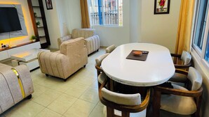 A modern living room with a round dining table, sofas, a TV mounted on the wall, and a chandelier. - Nyali Luxe 2BR • Beach - Parking - Peaceful, Safe (Mombasa)