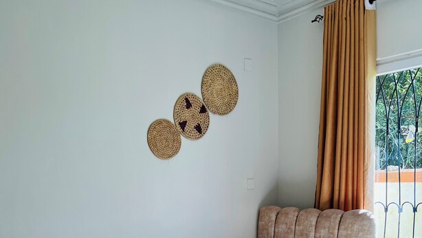 A single bed with a headboard, a small wall-mounted shelf with woven baskets, and a window with curtains. - Nyali Luxe 2BR • Beach - Parking - Peaceful, Safe (Mombasa)