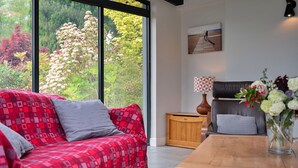 A modern living room with a red patterned sofa, a wooden side table, a black leather chair, and a painting on the wall. - Yonder Castle Hill (Harley)