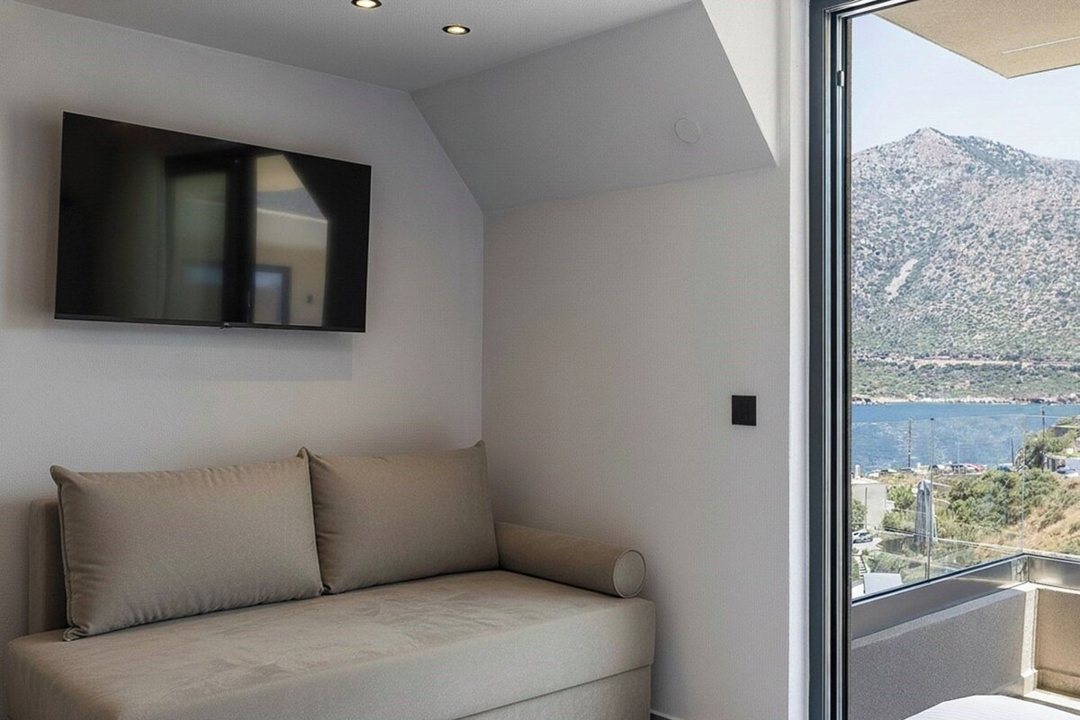 A modern room with a sofa, a mounted TV, and a balcony with a mountain view.