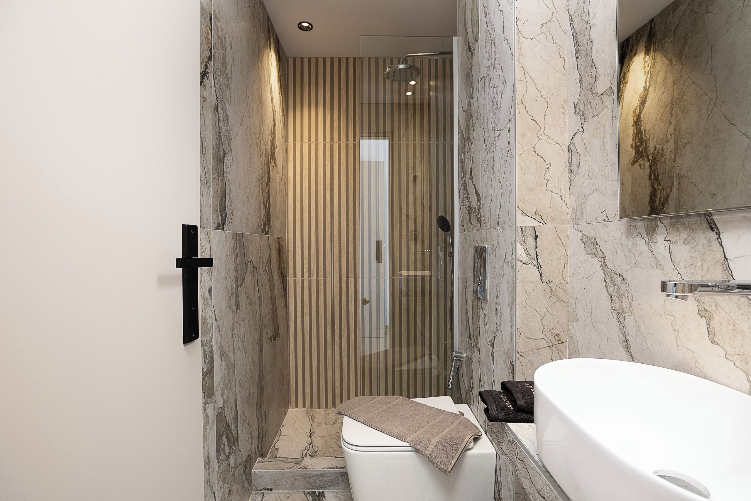 A modern bathroom with a marble wall, a glass shower enclosure, and a white bathtub.