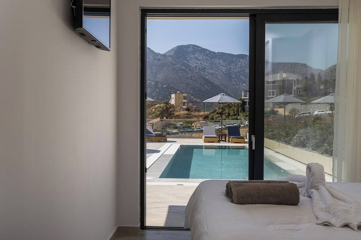A bedroom with a bed, a view of a swimming pool, and a mountain in the background.