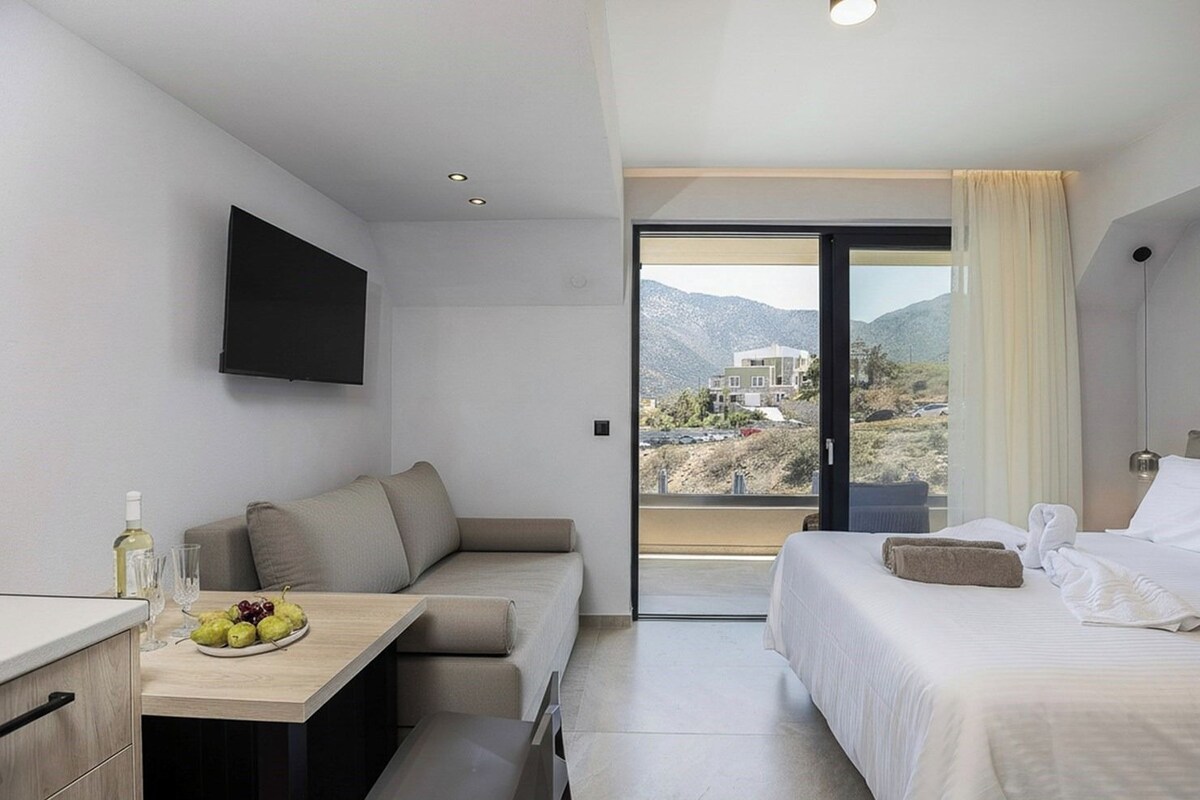 A modern hotel room with a sofa, a small table with fruit, a bed, and a TV.