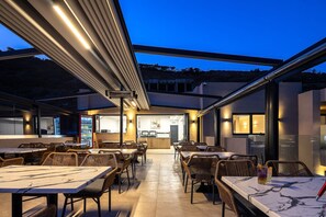 An outdoor dining area with tables and chairs, a bar, and a view of the landscape. - Celeste Bali Suites (Mylopotamos)