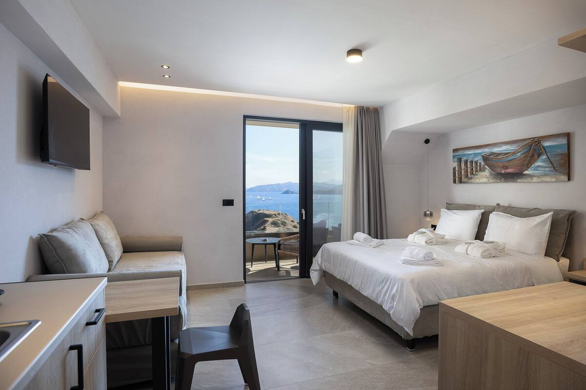 A modern hotel room with a bed, a desk, and a view of the sea.