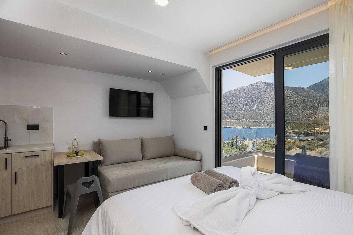 A modern hotel room with a bed, a desk, a sofa, and a large window with a mountain view.