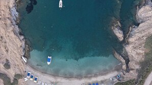 An aerial view of a coastal area with a beach, a boat, and a row of beach chairs. - Celeste Bali Suites (Mylopotamos)
