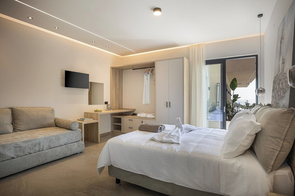 A modern hotel room with a bed, a sofa, a desk, a mirror, and a TV.