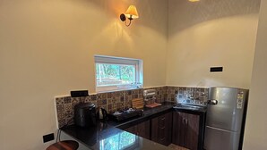 A compact kitchen with a central island, two stools, a window with a view, and a refrigerator. - Brahma Cottages (Canacona)