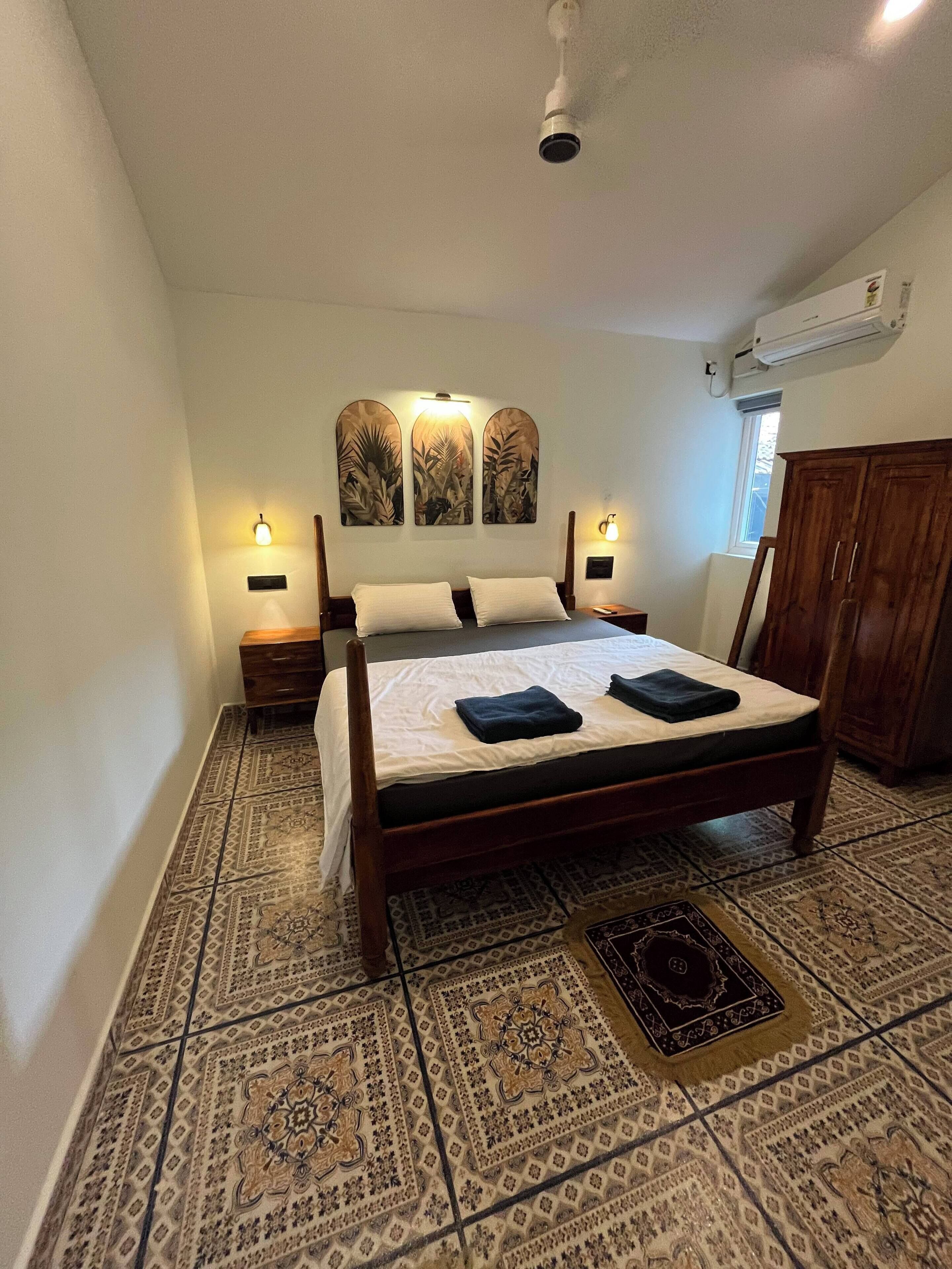 Un dormitorio con cama, baldosas de suelo con diseño, un armario de madera y obras de arte colgadas en la pared.