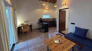 A cozy room with a thatched ceiling, a dining area with a small kitchen, a sofa, and a coffee table with a candle. - Brahma Cottages (Canacona)
