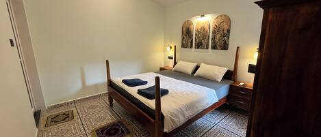 A bedroom with a wooden bed, patterned floor tiles, and a nightstand with a lamp.