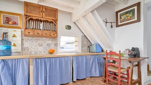 A kitchen with a wooden cabinet, a blue checkered tablecloth, a red chair, and a kettle on the counter. - Cortijo Palomo: Country House with Private Pool and Mountain Views (Málaga)
