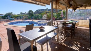 An outdoor patio with a pool, dining area, and a view of a hilly landscape. - Cortijo Palomo: Country House with Private Pool and Mountain Views (Málaga)