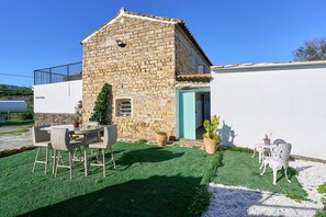 A stone building with a balcony, a table with chairs, and a small garden area. - Cortijo Palomo: Country House with Private Pool and Mountain Views (Málaga)