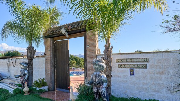A building entrance with a sign reading 'CORTIJNO PALOMO,' a brick wall, and two statues of a bull and a goose. - Cortijo Palomo: Country House with Private Pool and Mountain Views (Málaga)