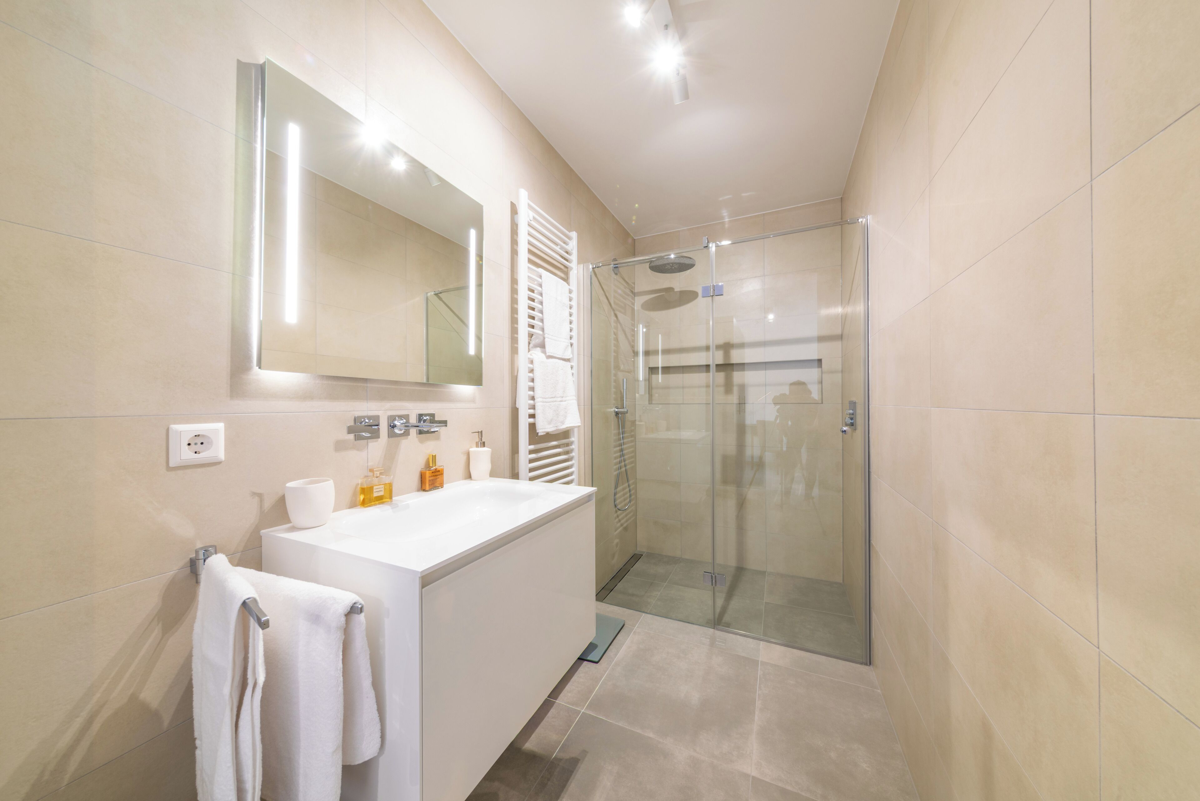 A modern bathroom with a glass-enclosed shower, a white sink, and a large mirror.