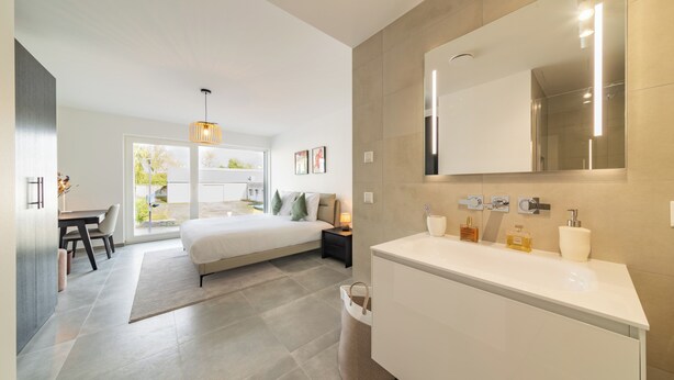 A modern bedroom with a large bed, bedside tables, a desk, and a view of the outdoors. - Halternative Muscari (Luxembourg City)