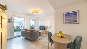 A modern living room with a grey sofa, a dining table with chairs, a TV, and a large window. - Halternative Muscari (Luxembourg City)