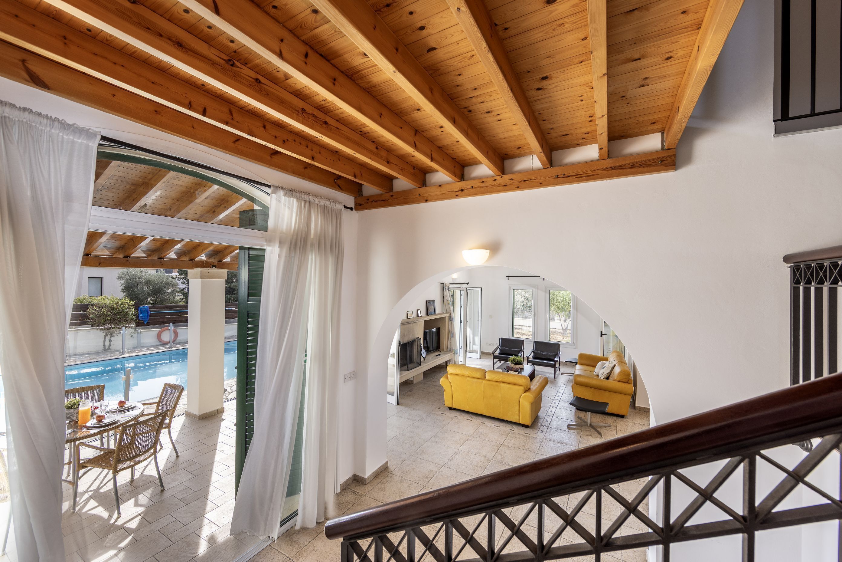 Un salón amplio con un sofá amarillo, una mesa de comedor con sillas y vistas a una piscina a través de un arco abierto.