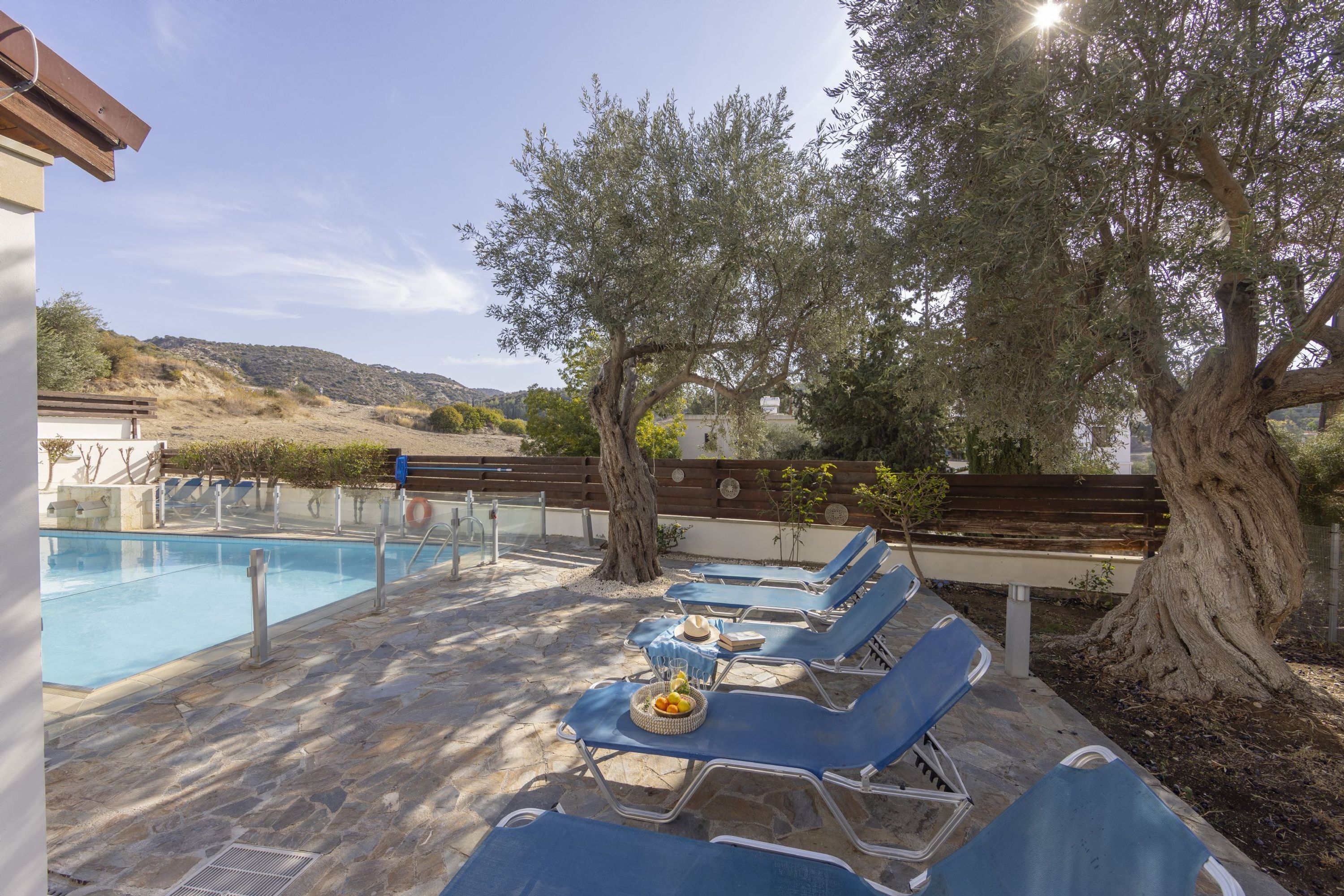 A poolside area with lounge chairs, a table with a basket of fruit, and a large tree.