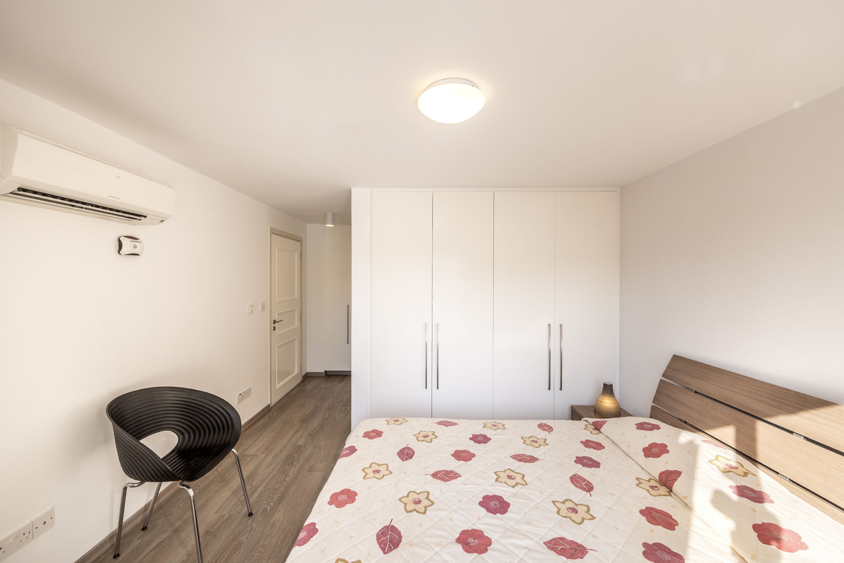 A bedroom with a bed, a chair, a wardrobe, and an air conditioning unit.