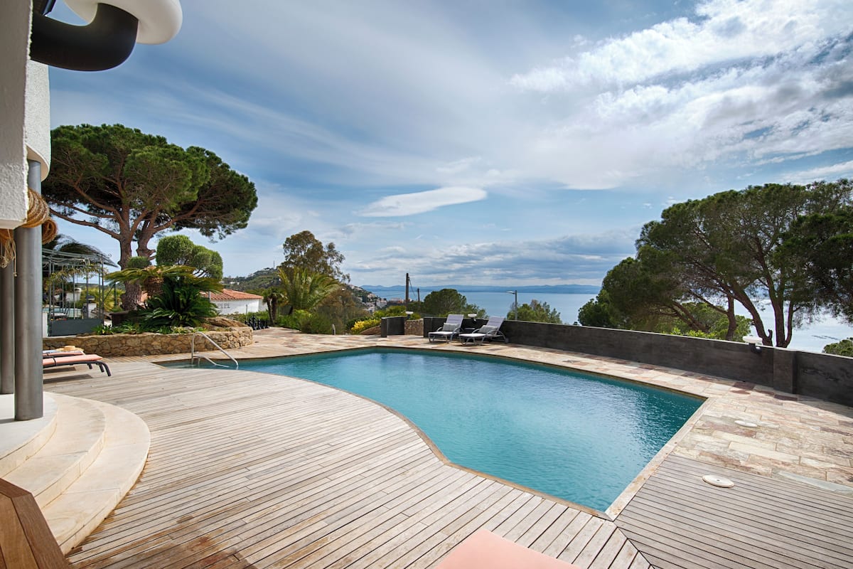 Une terrasse en bois avec une piscine, des chaises longues et une vue sur la mer.