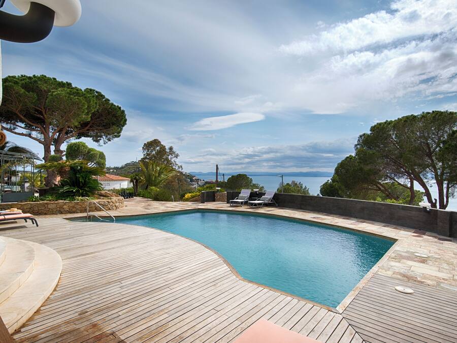 Eine Holzterrasse mit Swimmingpool, Liegestühlen und Meerblick.
