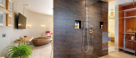A modern bathroom with a glass shower enclosure, a large bathtub, and a sink area with a potted plant.