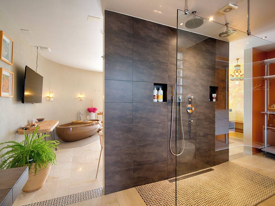 A modern bathroom with a glass shower enclosure, a large bathtub, and a sink area with a potted plant.