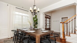 A dining room with a wooden table, black chairs, a chandelier, and a staircase. - Spacious Family Home | 4BR | Fenced Yard | WR (Warner Robins)