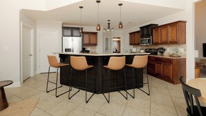A modern kitchen with a central island, bar stools, and wooden cabinetry. - Spacious Family Home | 4BR | Fenced Yard | WR (Warner Robins)