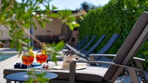 Et loungeområde ved poolen med to glas rød drik, en tallerken med dessert og et lille bord.