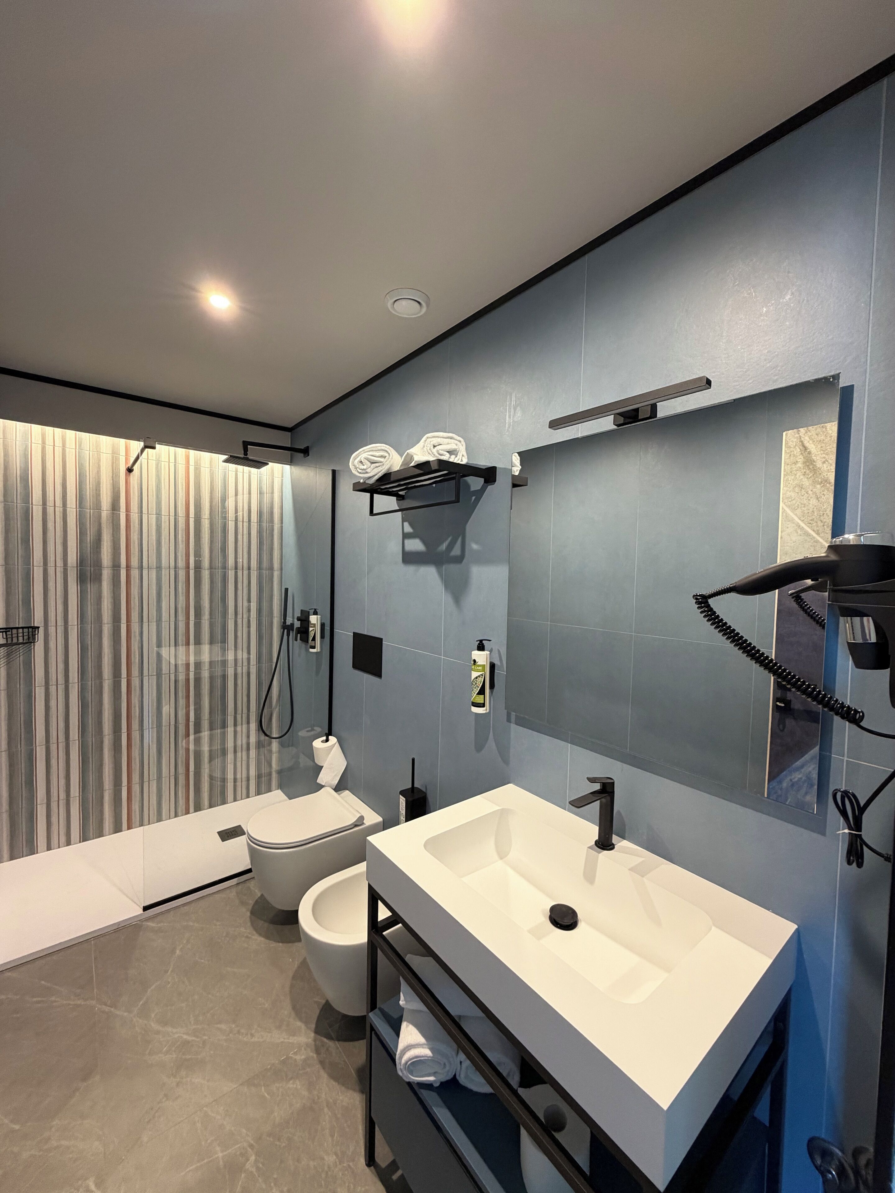 Une salle de bain moderne avec un grand miroir, un lavabo blanc, des toilettes et un espace douche.