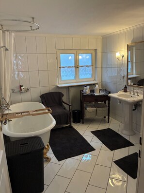 Een badkamer met een bad, een wastafel, een stoel en een raam met geëtste ruiten.