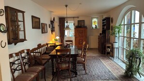 A dining area with a wooden table and chairs, a patterned rug, and a large window with a view of the outside. - Large, comfortable half-timbered house with courtyard in the heart of Wissembourg (Wissembourg)