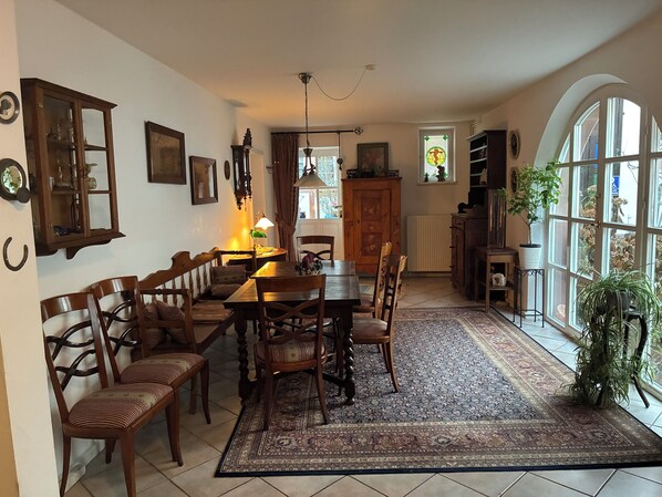 Een eetgedeelte met een houten tafel en stoelen, een kamerkleed met een patroon, en een groot raam met uitzicht.
