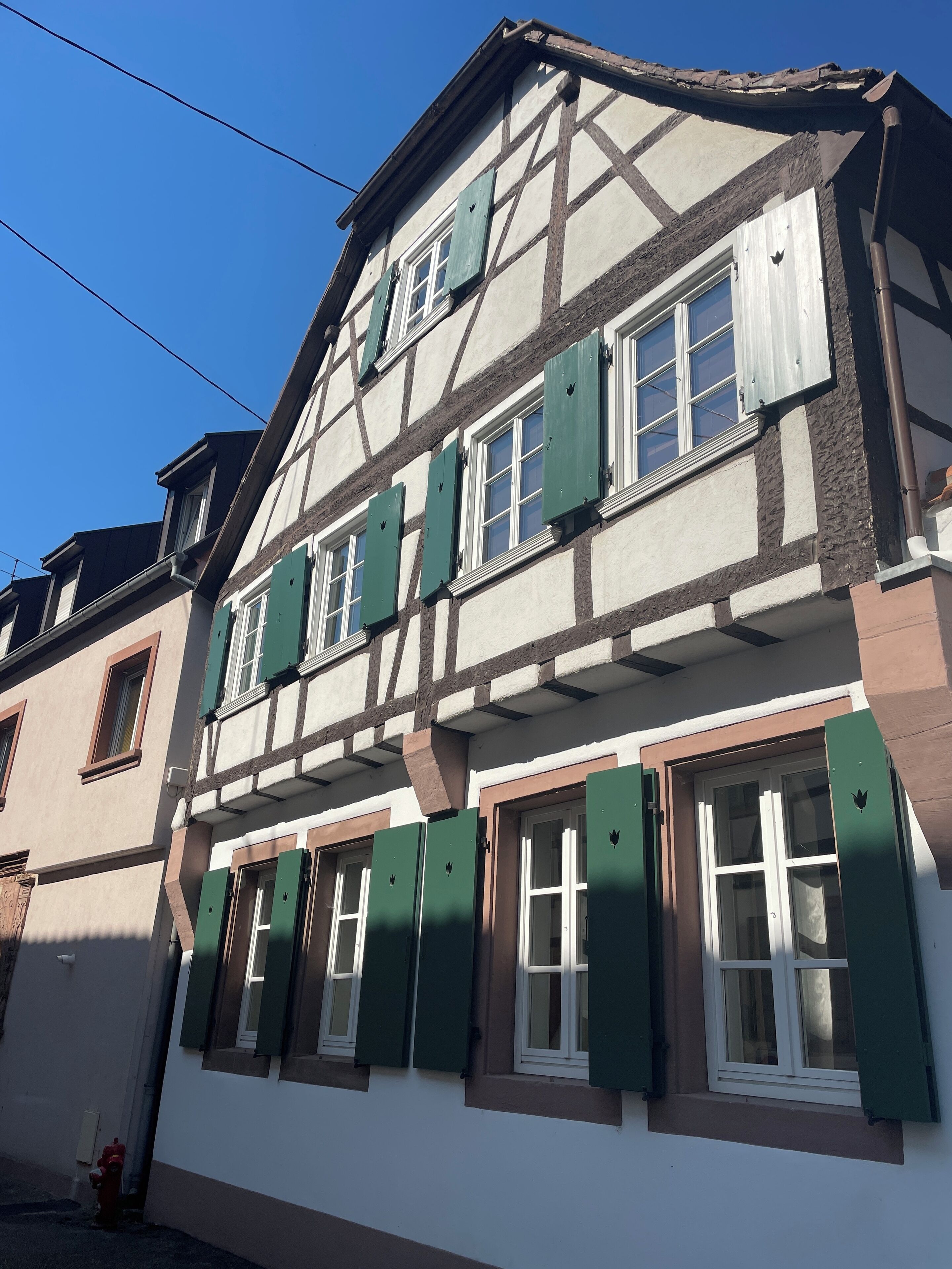 Un bâtiment traditionnel à colombages, doté de nombreuses fenêtres et de volets verts.
