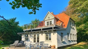 Ein zweistöckiges Haus mit Balkon, überdachter Terrasse und Rasen.