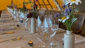 Ein mit Zeltdach gedeckter Essbereich mit gedeckten Tischen, bestecktem Geschirr und floralen Tischdekorationen.